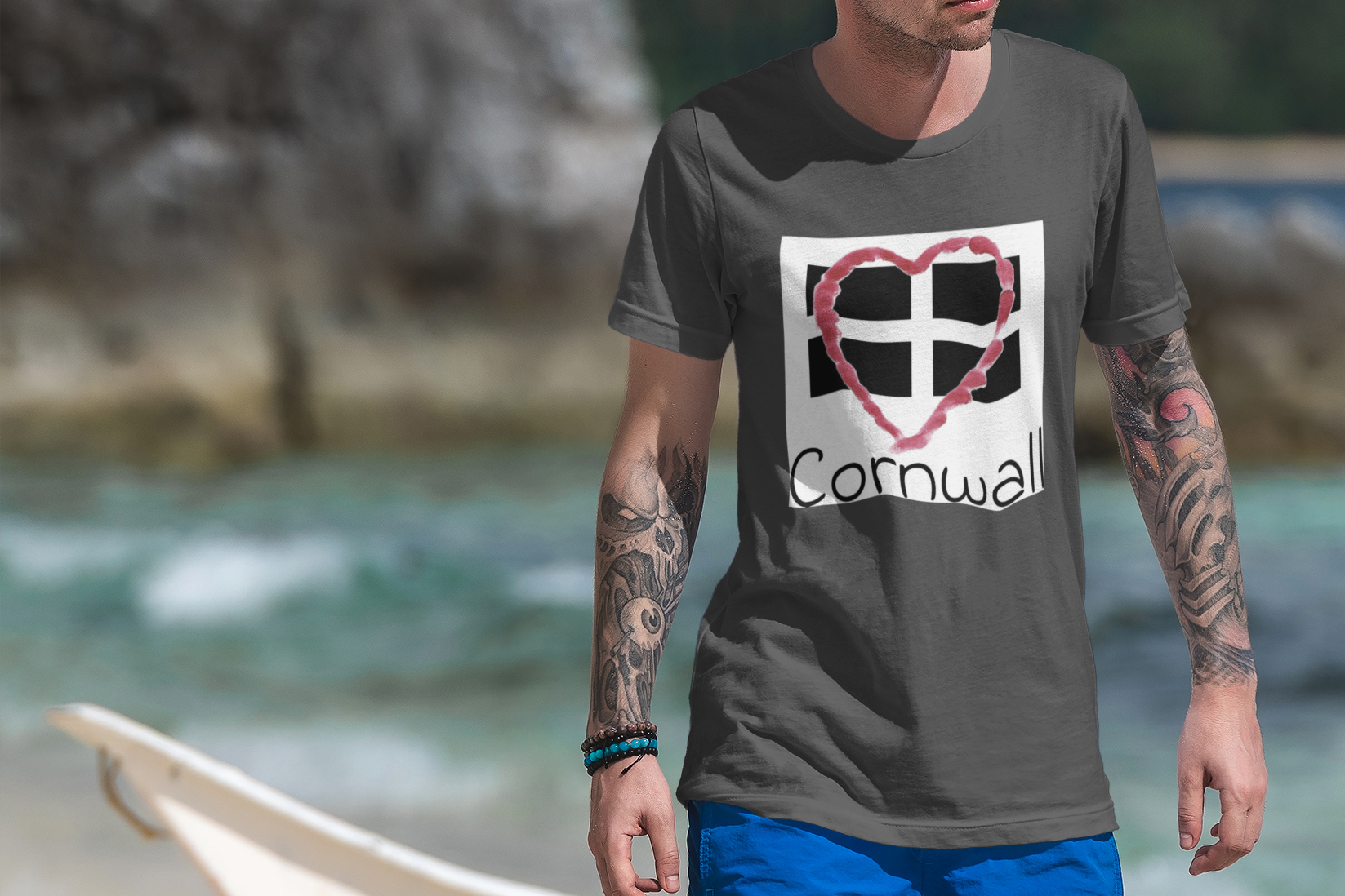 Man wearing Asphalt Cornwall Heart Flag t-shirt on rocky Cornwall beach
