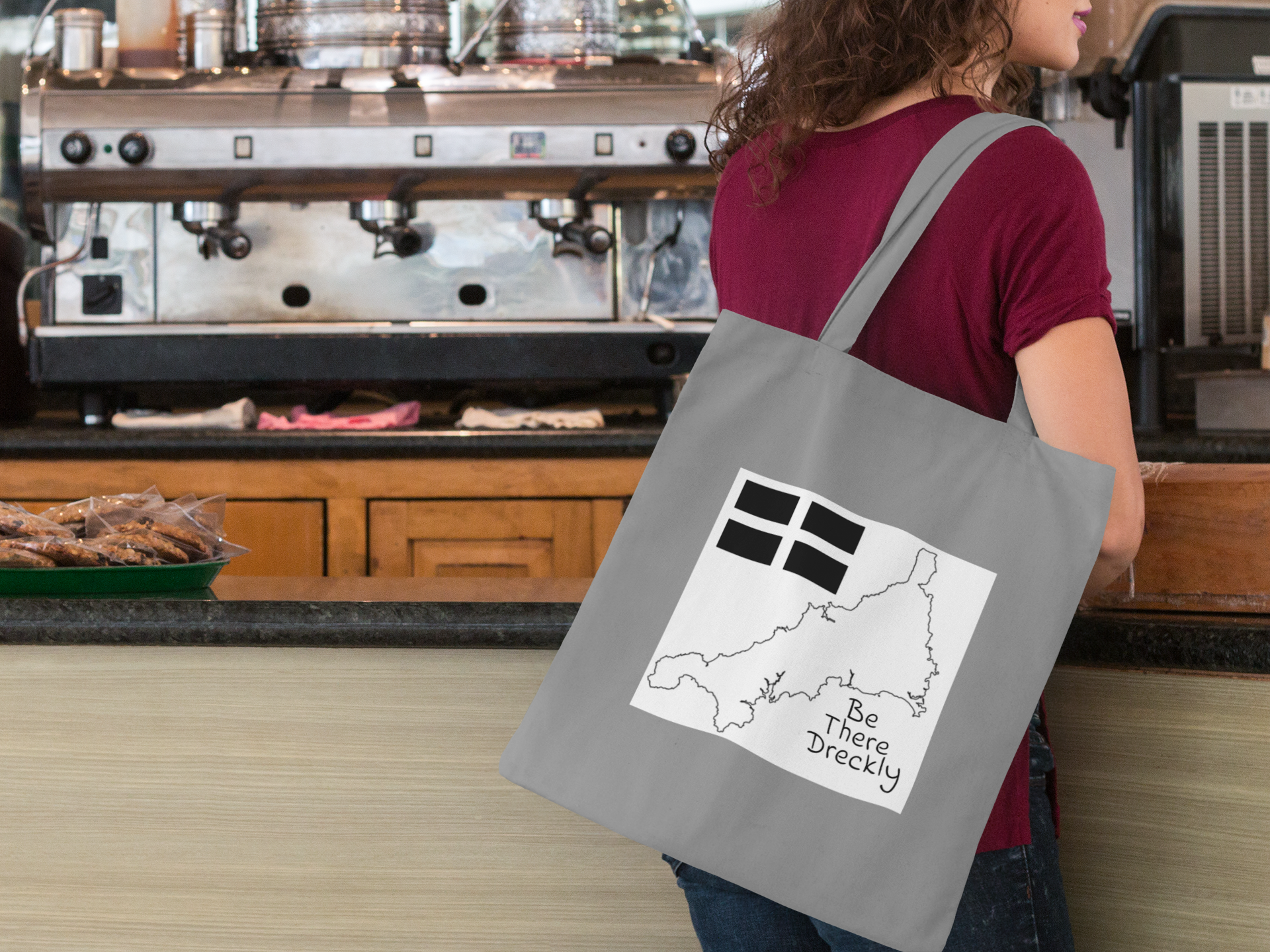 Woman carrying Cornish dialect tote bag over shoulder in café — Cornwall gift shopper