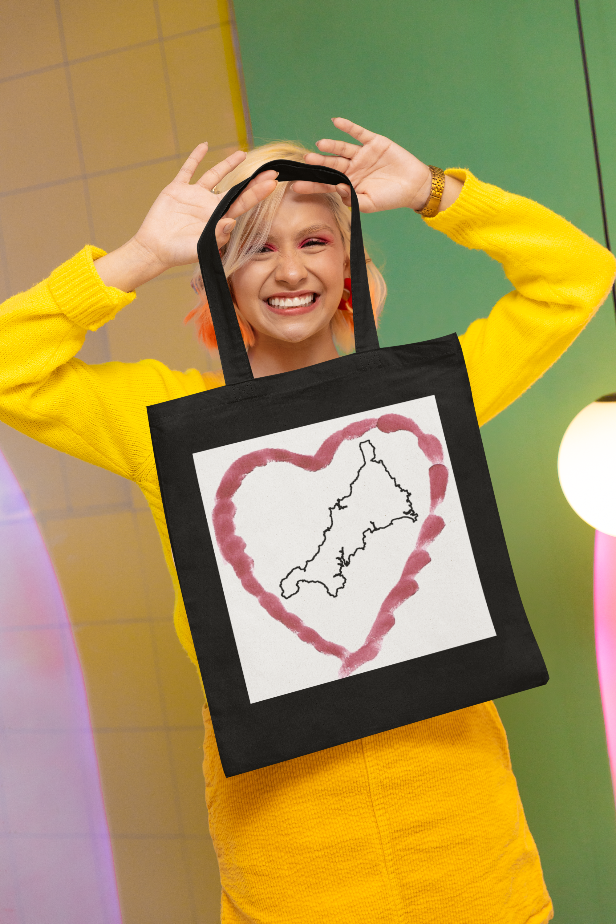 Woman, smiling while holding Black I Love Cornwall tote bag — Kernow heart map cotton gift shopper
