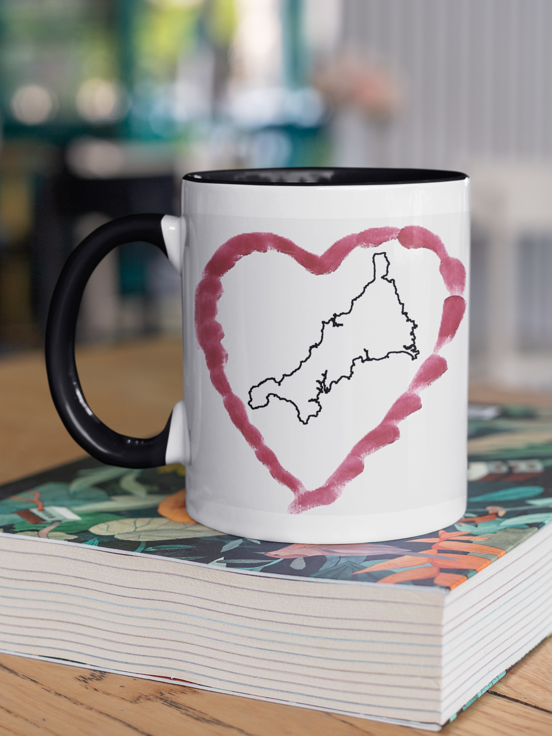I Love Cornwall heart map mug with black handle on patterned book, Cornwall outline design