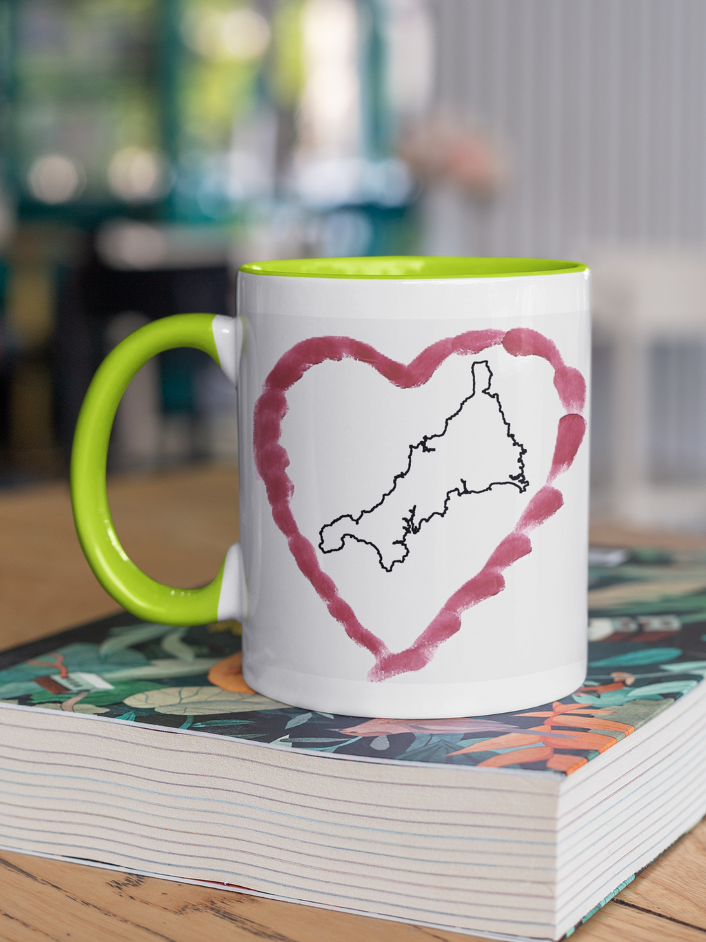 I Love Cornwall heart map mug with green handle on patterned book, Cornwall outline design