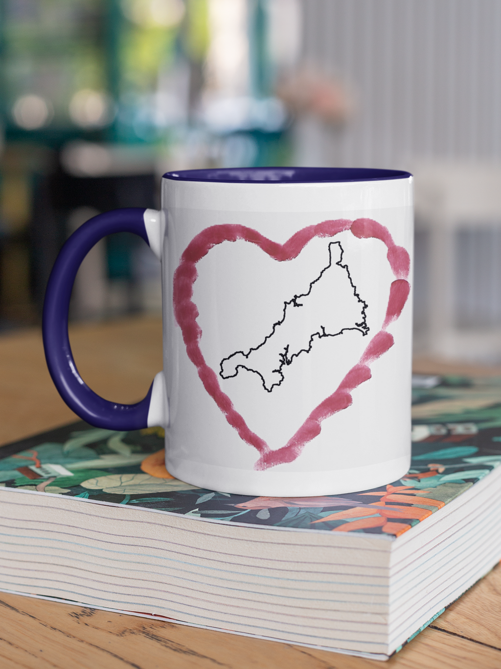 I Love Cornwall heart map mug with navy handle on patterned book, Cornwall outline design
