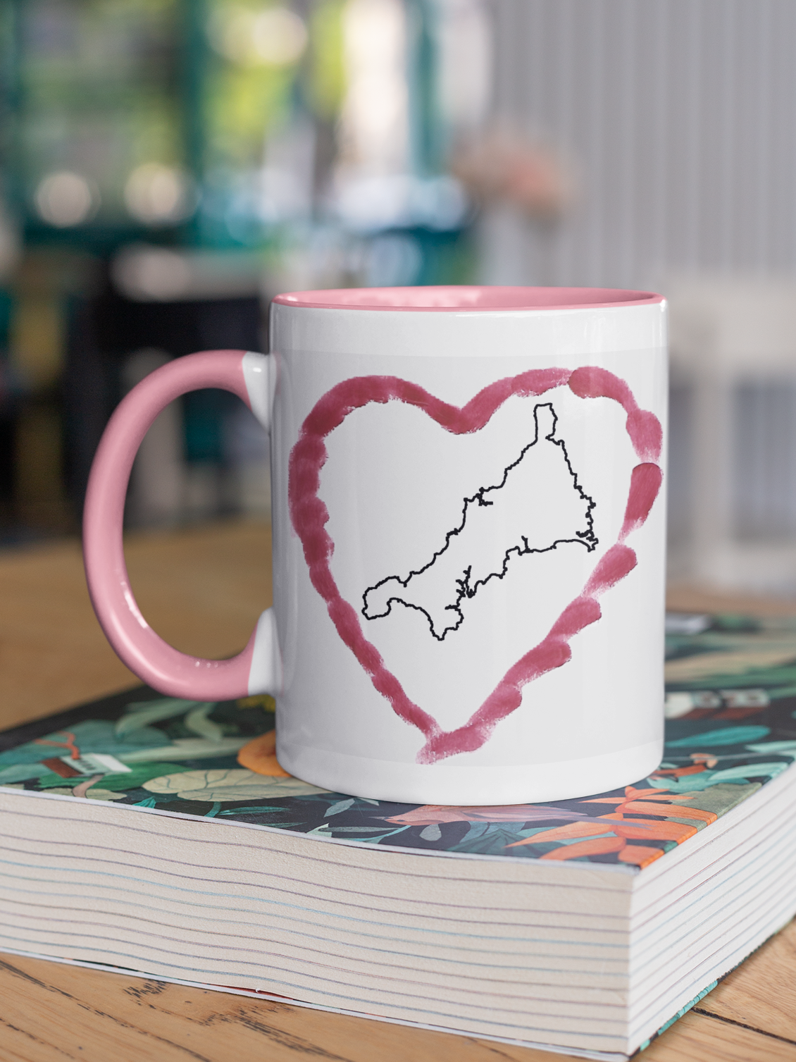 I Love Cornwall heart map mug with pink handle on patterned book, Cornwall outline design