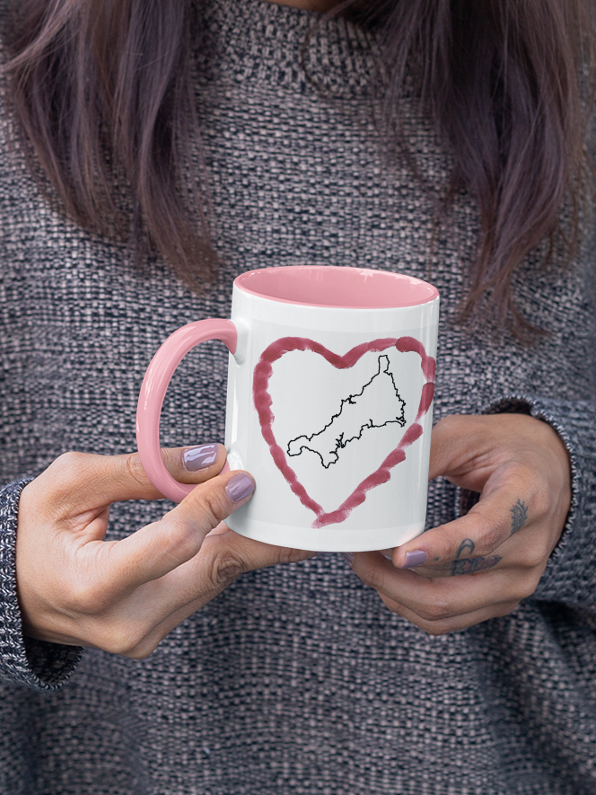 Hands holding I Love Cornwall heart map mug with pink handle, Cornwall outline design