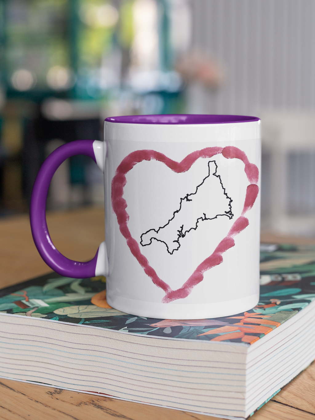 I Love Cornwall heart map mug with purple handle on patterned book, Cornwall outline design