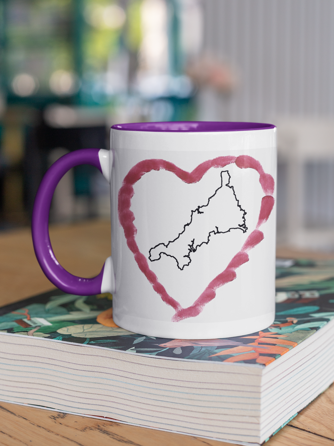 I Love Cornwall heart map mug with purple handle on patterned book, Cornwall outline design