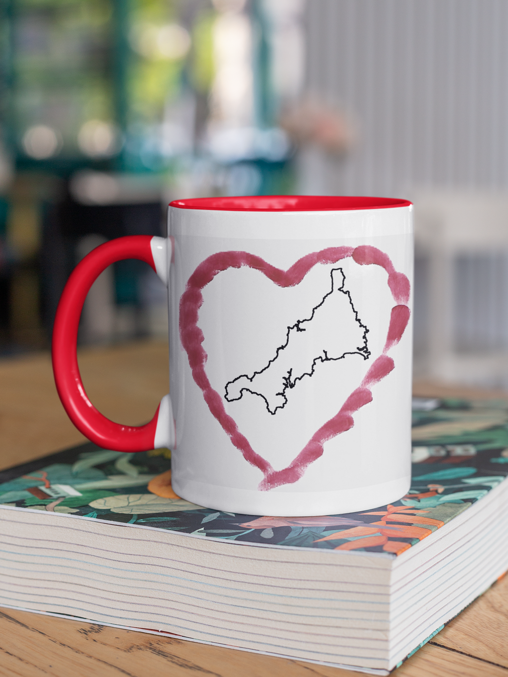 I Love Cornwall heart map mug with red handle on patterned book, Cornwall outline design