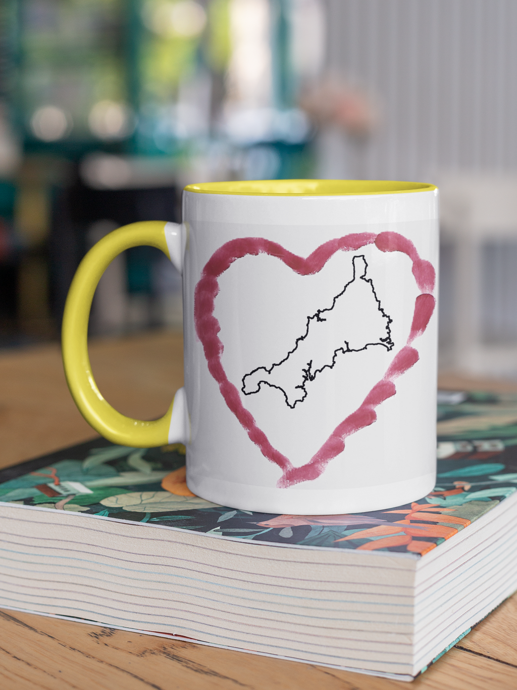 I Love Cornwall heart map mug with yellow handle on patterned book, Cornwall outline design