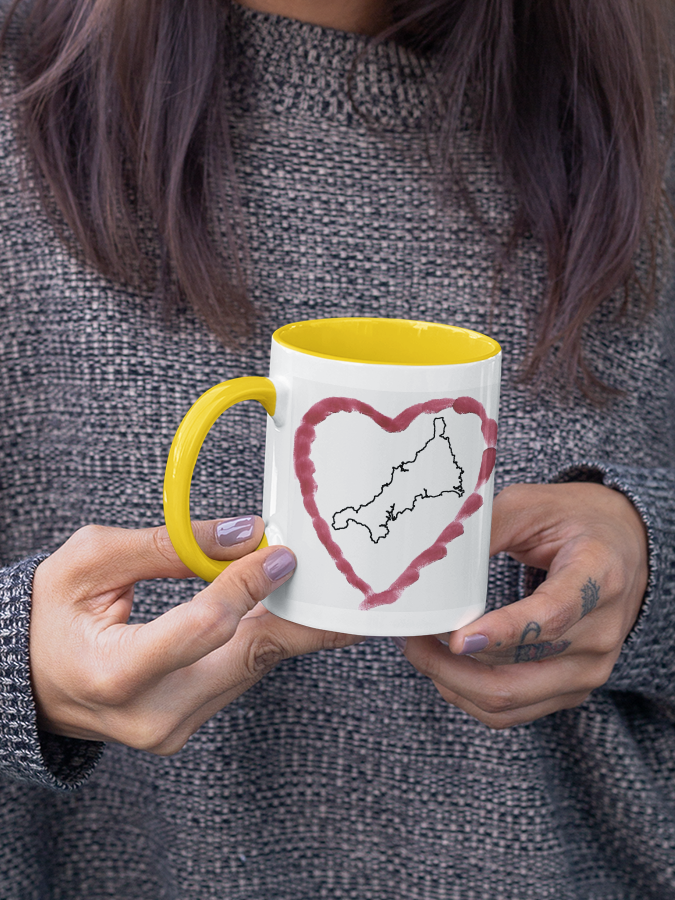 Hands holding I Love Cornwall heart map mug with yellow handle, Cornwall outline design
