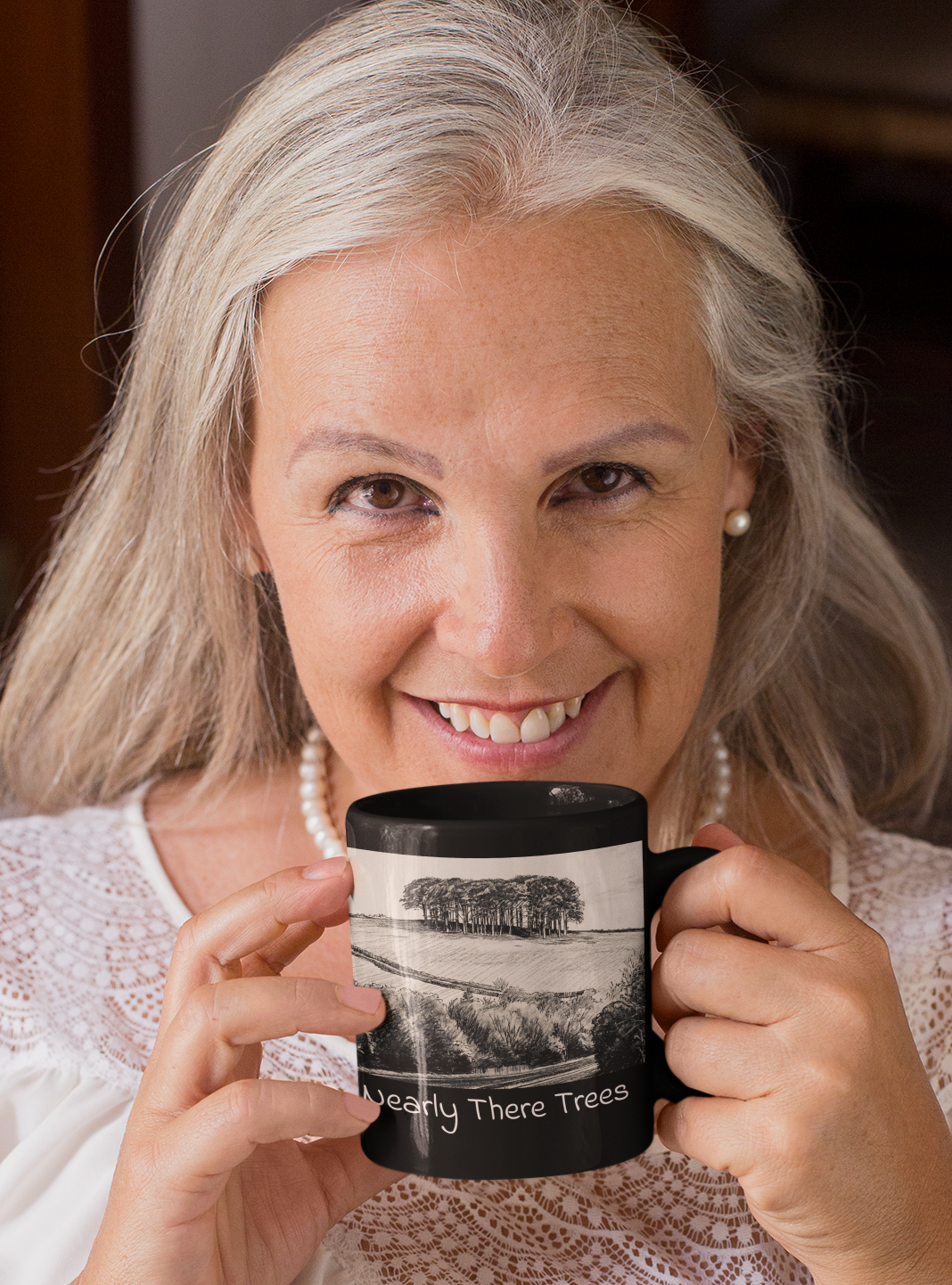 Woman with pearl necklace holding Nearly There Trees all-black mug, tree landscape pencil sketch design