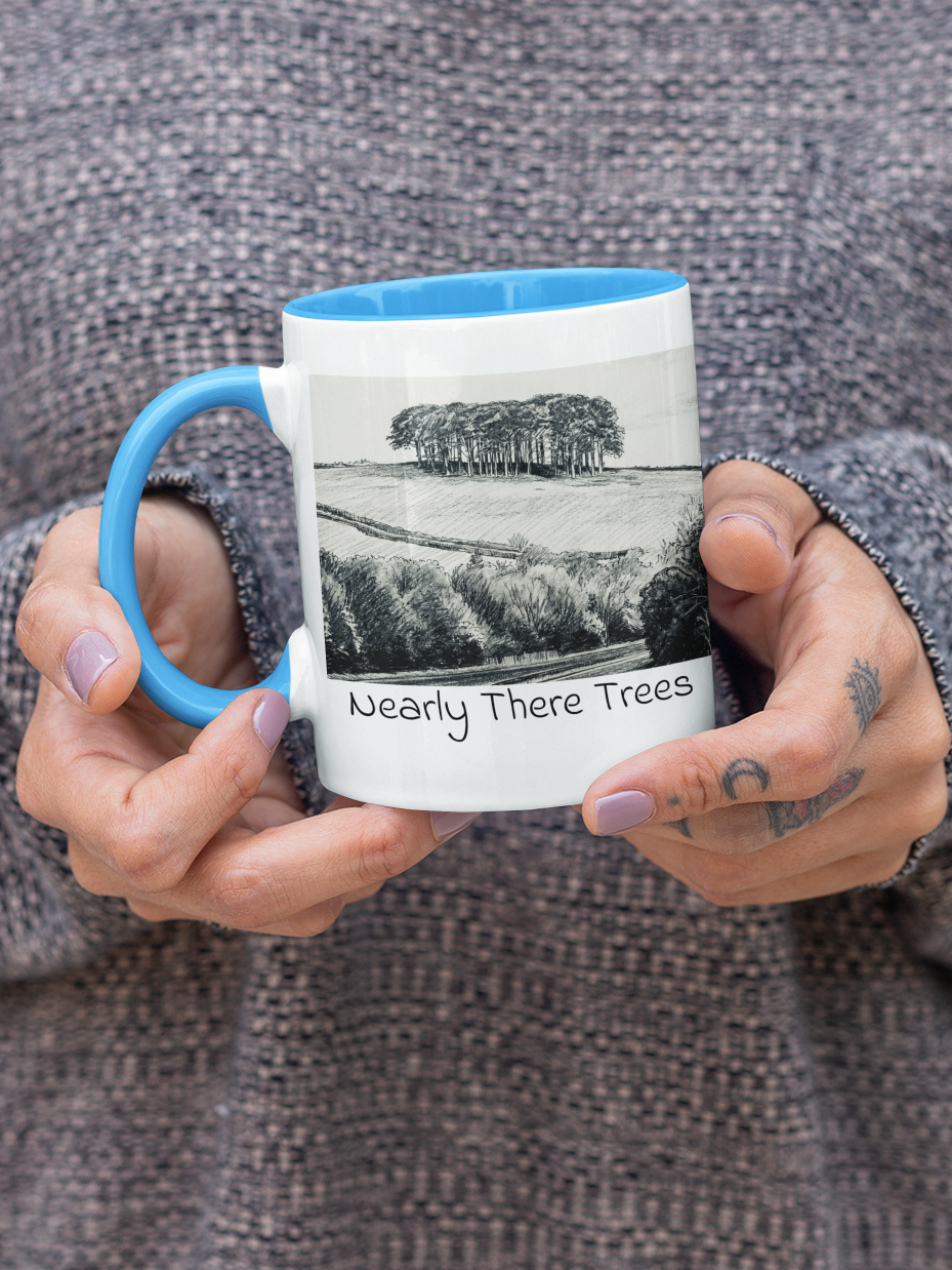 Hands holding Nearly There Trees mug with light blue handle, A30 Cornwall tree landscape pencil sketch design