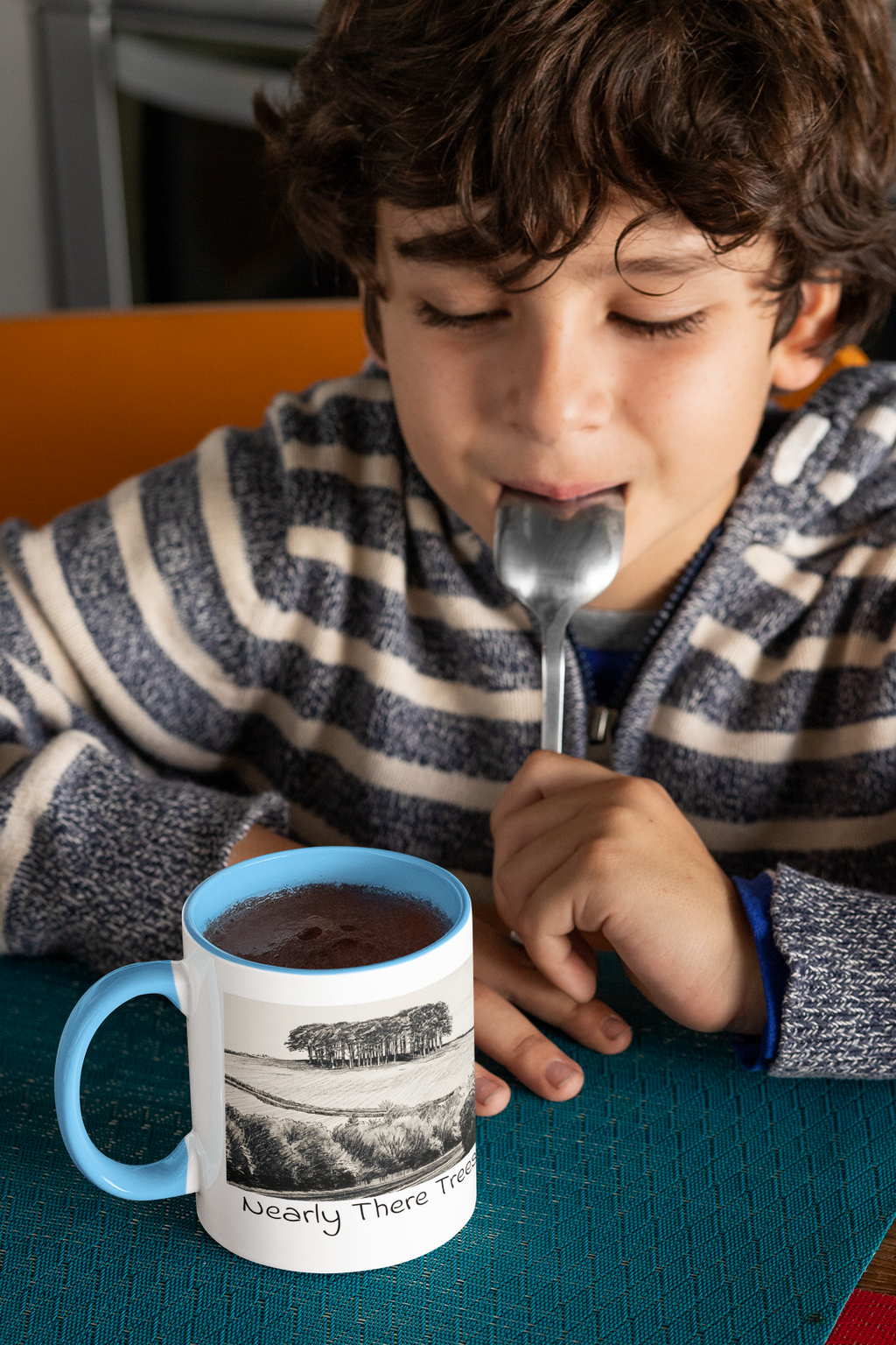 Child drinking hot chocolate beside Nearly There Trees mug with light blue handle, tree landscape sketch design
