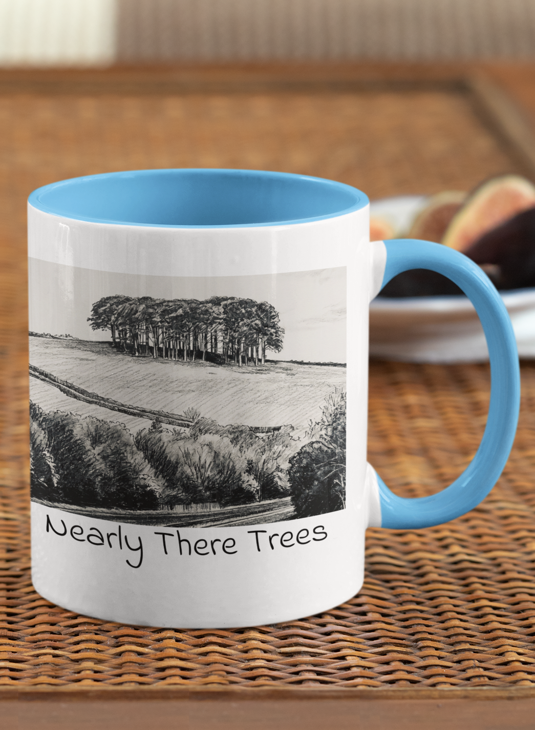 Nearly There Trees mug with light blue handle on wicker table, Cornwall tree landscape pencil sketch design