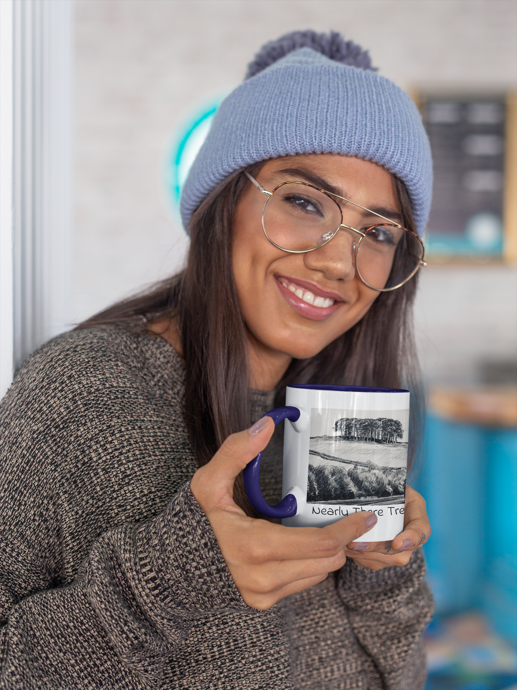 Woman in beanie holding Nearly There Trees mug with navy handle, tree line pencil sketch design