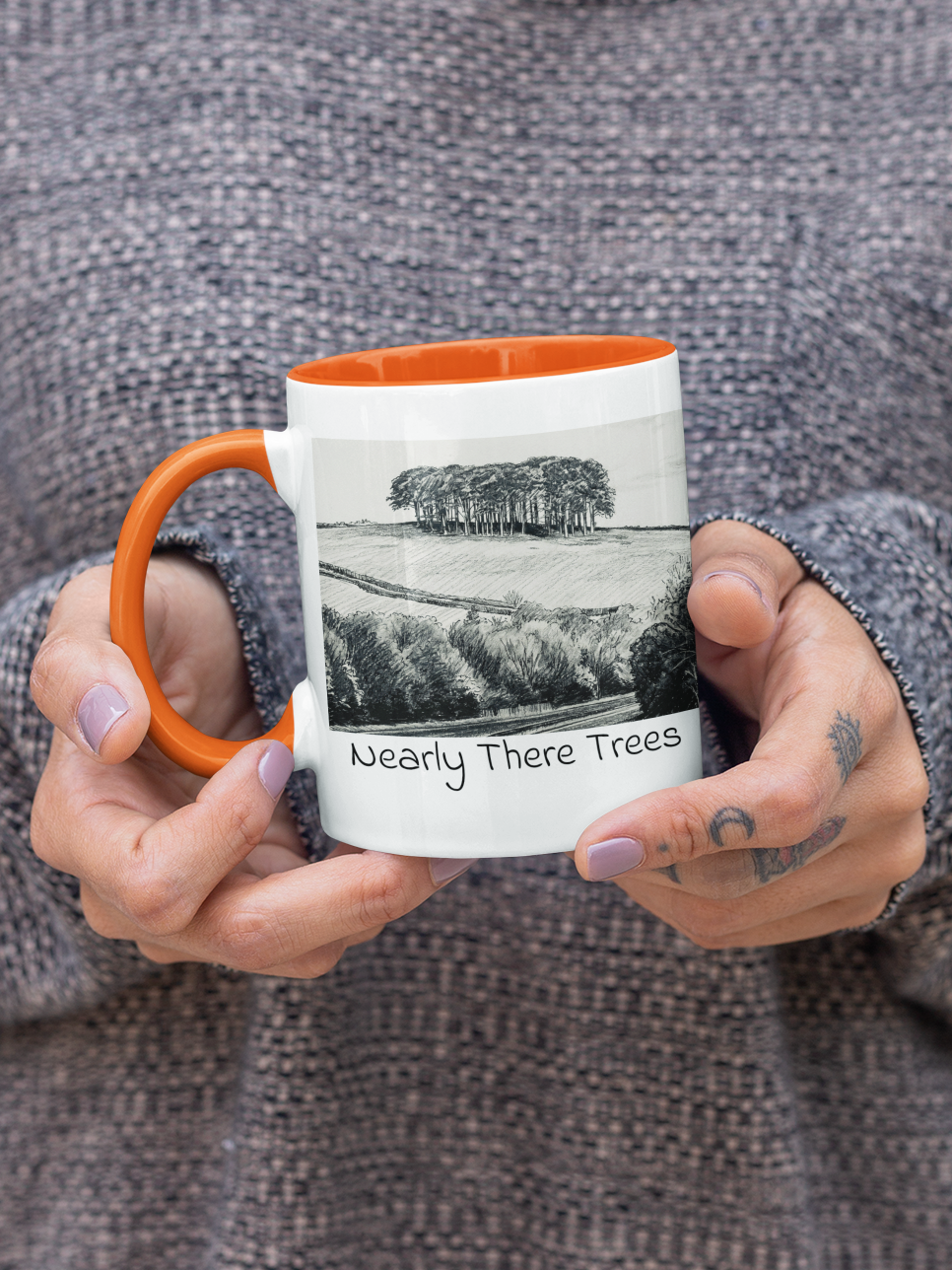 Hands holding Nearly There Trees mug with orange handle, A30 Cornwall tree landscape pencil sketch design