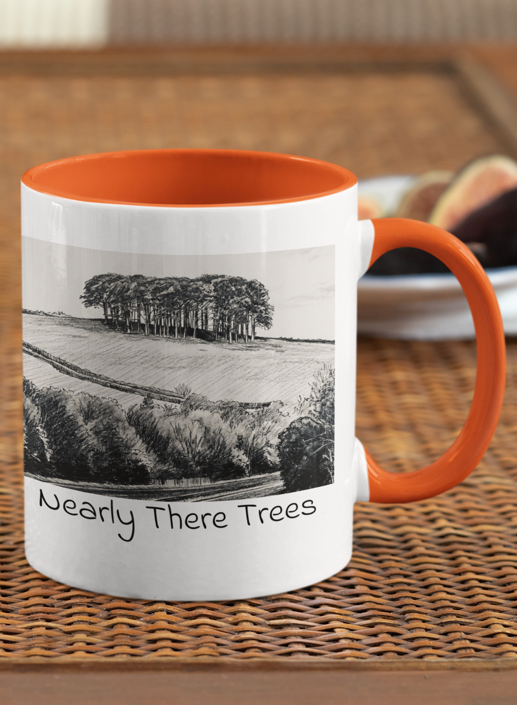 Nearly There Trees mug with orange handle on wicker table, Cornwall tree landscape pencil sketch design