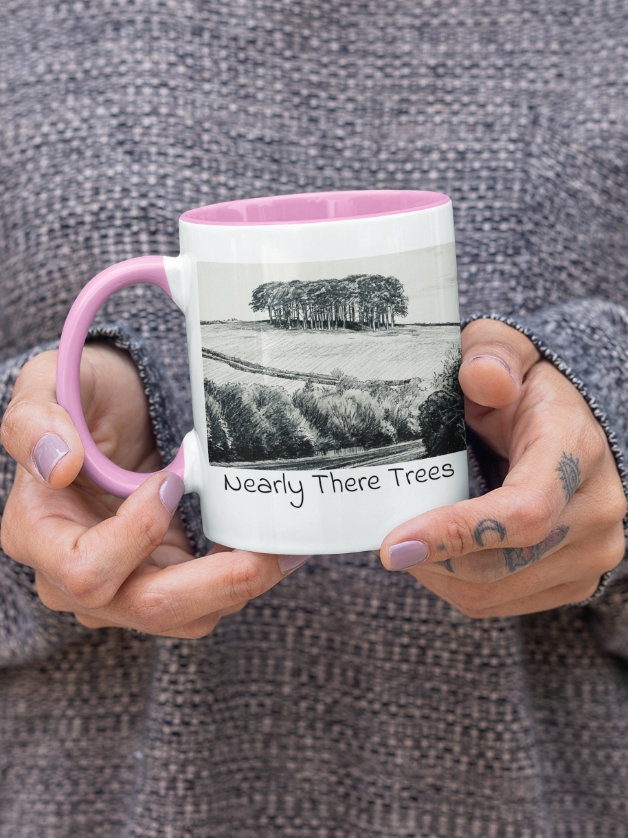 Hands holding Nearly There Trees mug with pink handle, A30 Cornwall tree landscape pencil sketch design