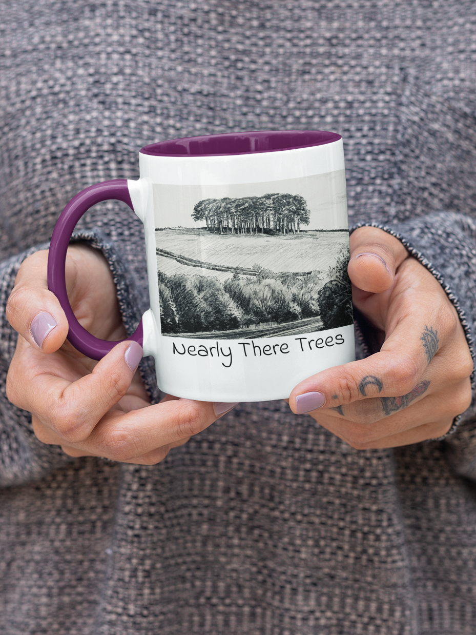 Close-up of hands holding Nearly There Trees mug with purple handle, tree landscape pencil sketch design