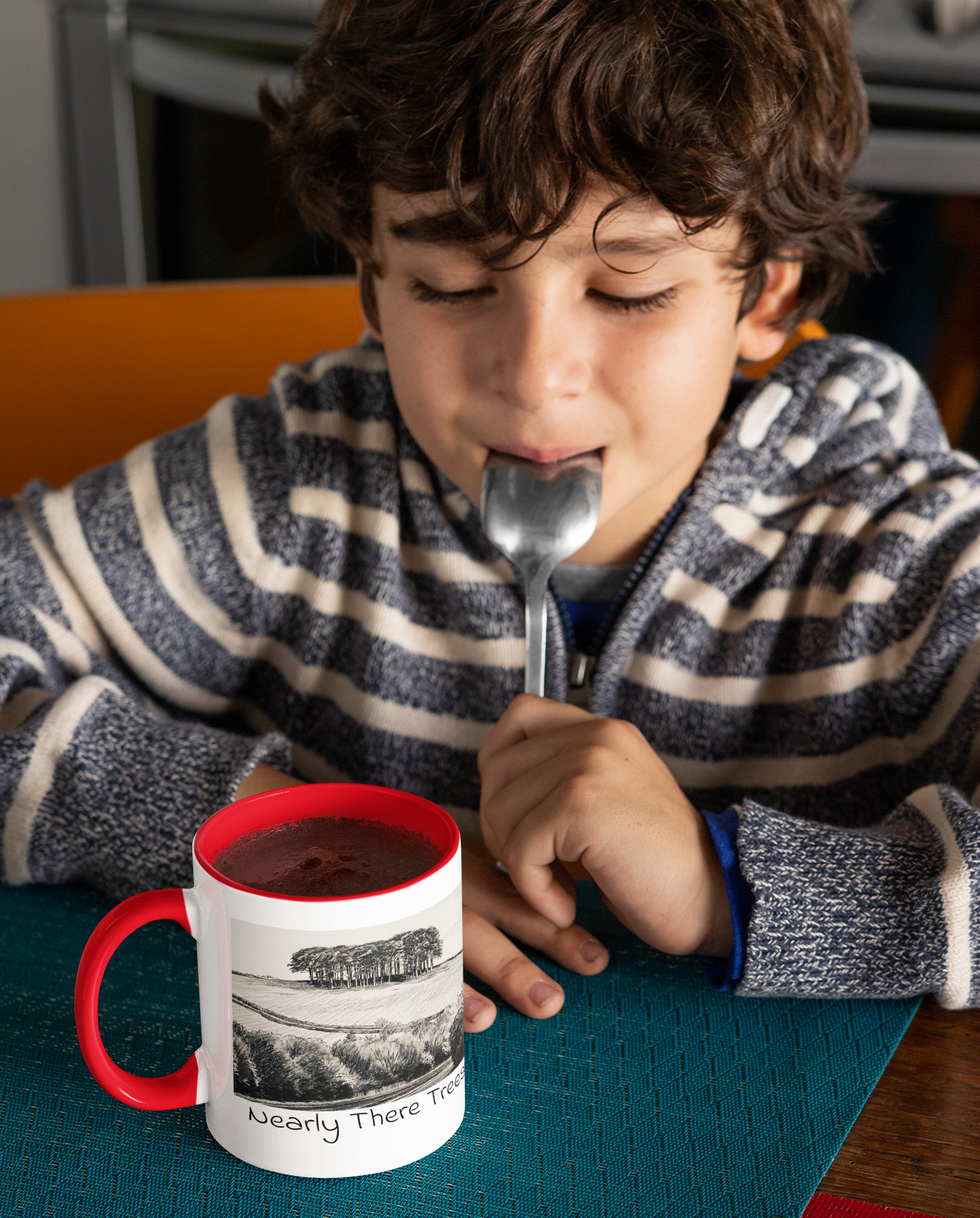 Child drinking hot chocolate beside Nearly There Trees mug with red handle, tree landscape sketch design