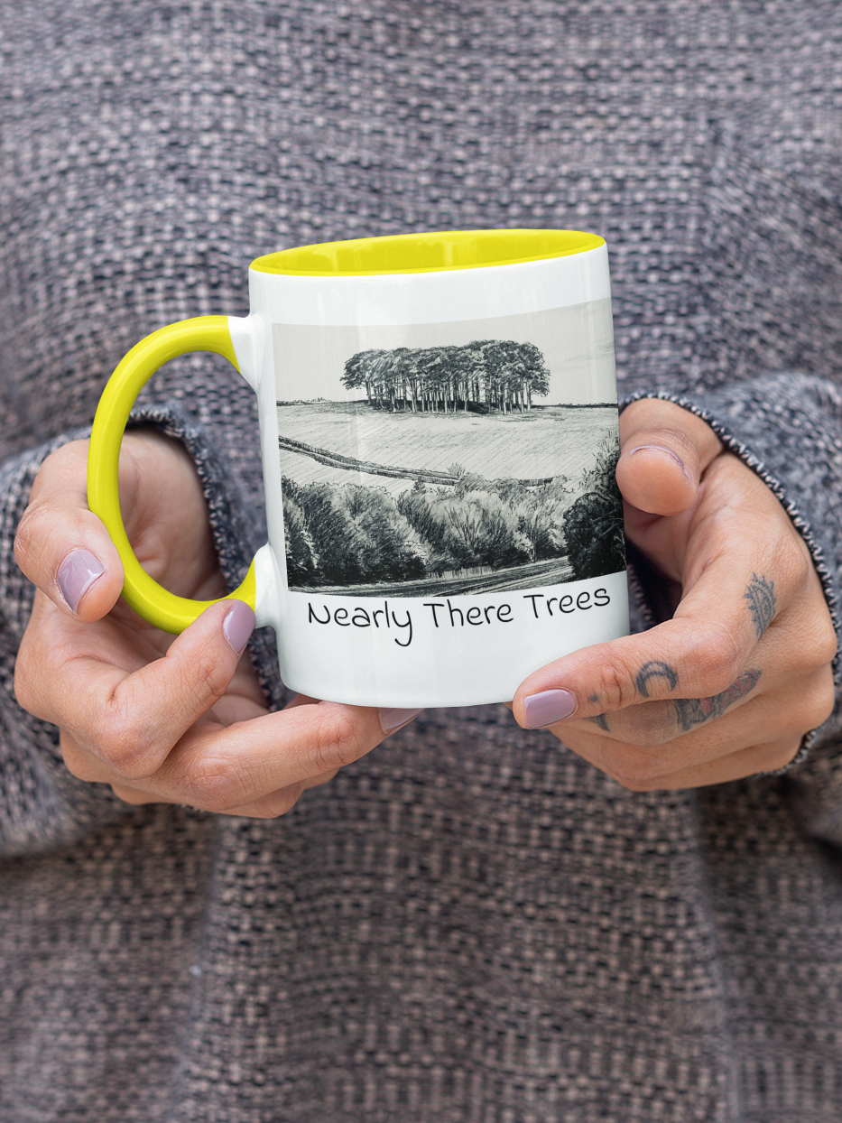Hands holding Nearly There Trees mug with yellow handle, A30 Cornwall tree landscape pencil sketch design