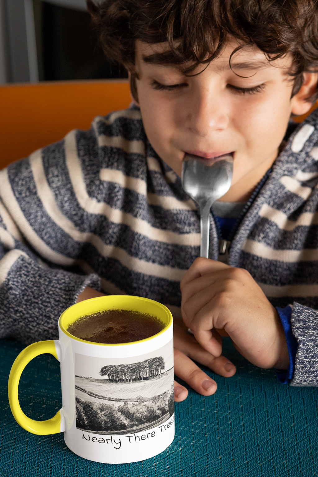 Boy with spoon beside Nearly There Trees mug with yellow handle and hot chocolate, tree sketch design