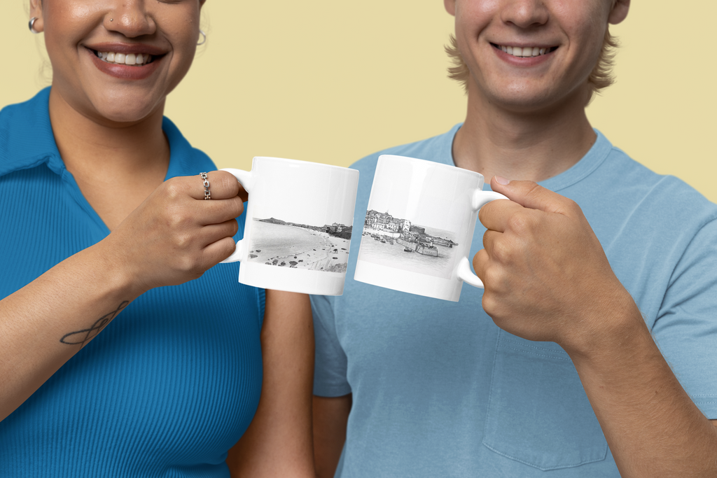 Couple cheersing St Ives Cornwall mugs showing beach and harbour illustrations, yellow background lifestyle shot