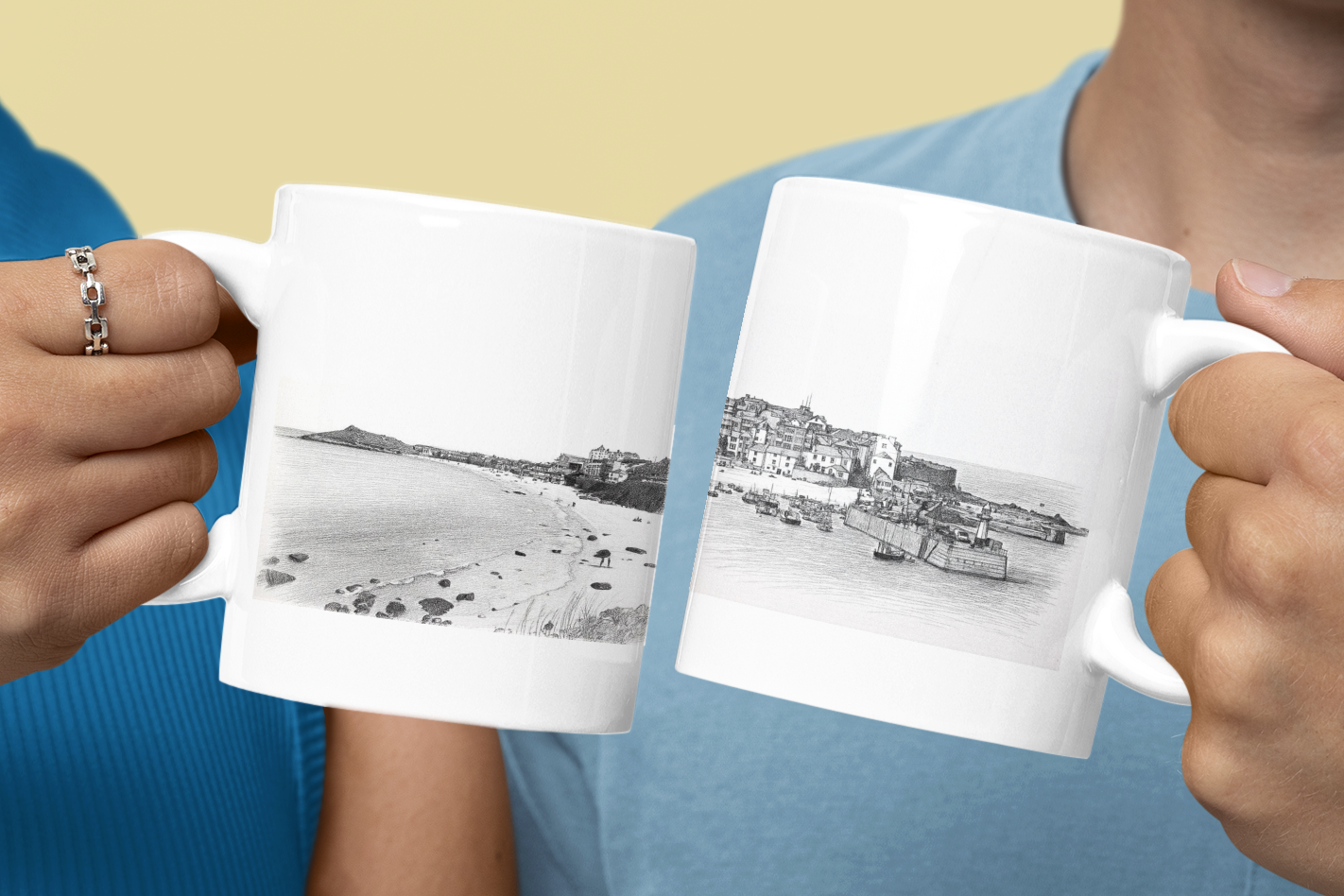 Couple holding St Ives Cornwall mugs showing Porthmeor Beach and harbour pencil sketch designs, ceramic coffee mugs